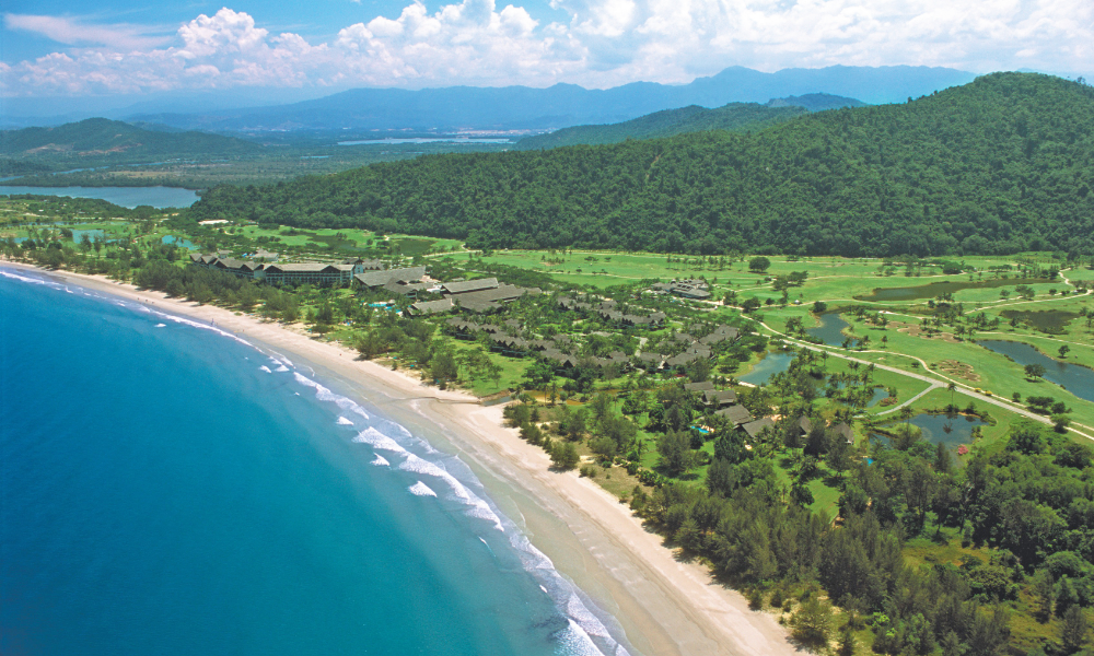 Aerial view of a beautiful beachfront resort with a vast beach and surrounding hills.