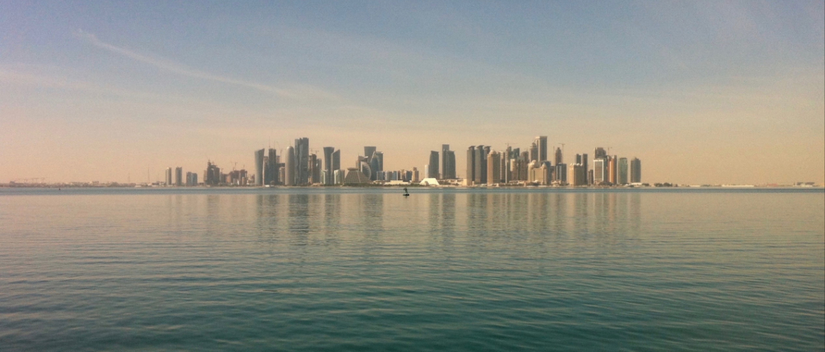 City of Doha as seen from the ocean, a lone paddle-boarder is on the glass calm sea. 