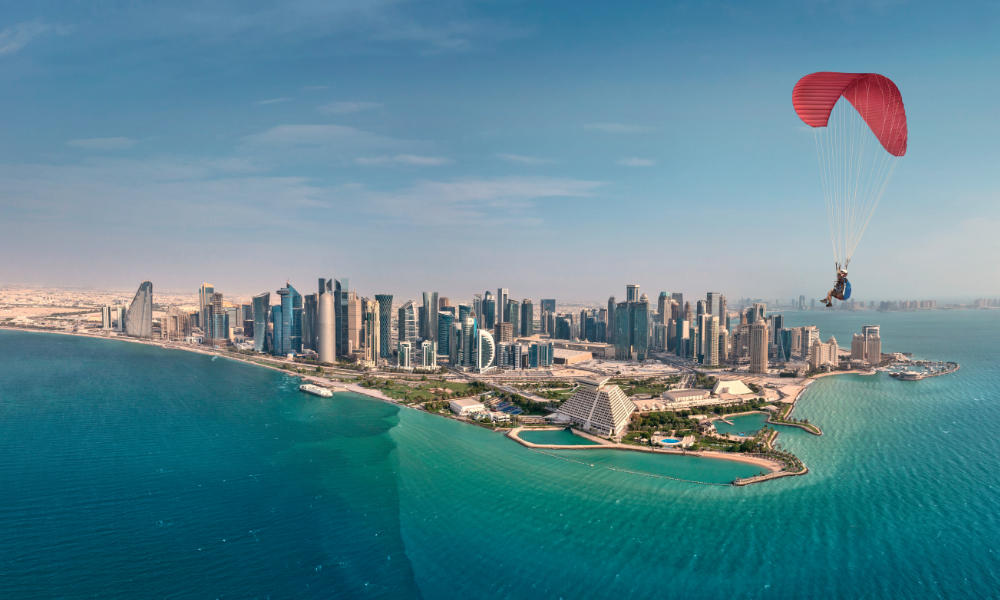 Parachutist flying over bay with clear blue skies and Doha in the background