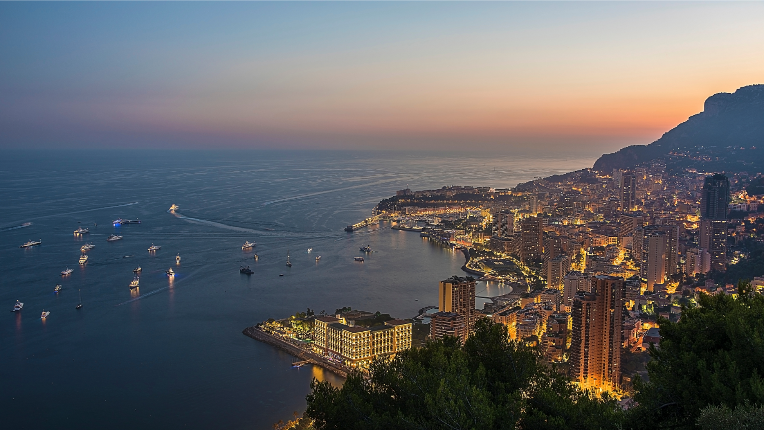 View from the hills above Monaco at dusk with glowing lights. The first destination-on this Monte Carlo Cruise